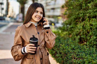 Genç, güzel, esmer bir kadın dışarıda mutlu bir şekilde gülümsüyor telefonda konuşuyor.