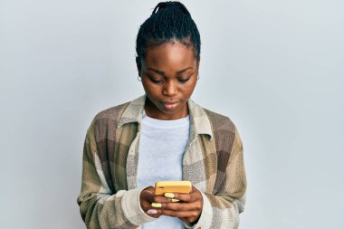 Genç Afro-Amerikan kadın akıllı telefon kullanıyor. Yüzünde ciddi bir ifade var. Basit ve doğal bir şekilde kameraya bakıyorsun.. 