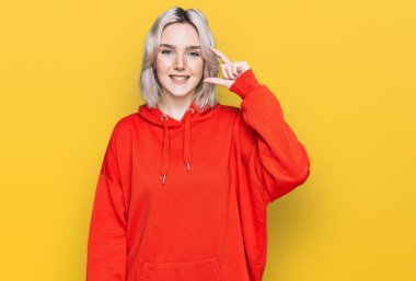 Gündelik kıyafetler giyen, gülümseyen, kendine güvenen, el hareketleriyle küçük boy işareti yapan, parmaklarıyla işaret eden ve kameraya bakan genç sarışın kız. ölçüm kavramı. 