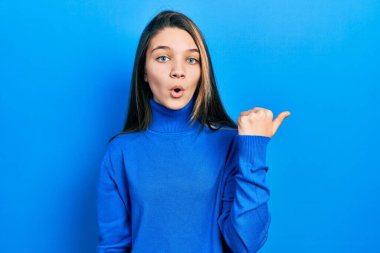 Balıkçı yaka kazak giyen genç esmer kız elleri yana dönük, ağzı açık şaşkın bir ifadeyle şaşırdı.. 