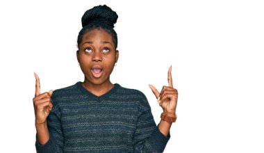 Genç Afrikalı Amerikalı kadın gündelik kıyafetler giyip şaşkın şaşkın yukarı bakıyor ve parmaklarıyla işaret ediyor ve kollarını kaldırıyor.. 
