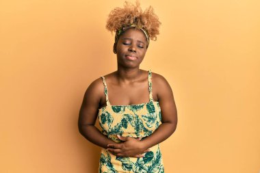 Afro saçlı, yaz elbisesi giymiş, midesi üstünde genç bir Afrikalı kadın. Çünkü hazımsızlık, acı verici bir hastalık ve kendini iyi hissetmiyor. Ağrı kavramı. 