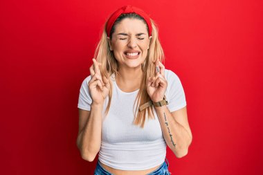 Beyaz günlük tişörtler giyen genç beyaz kadın umut ve gözlerin kapalı gülümseyerek parmaklarını çapraz yaptı. Şans ve batıl inançlar. 