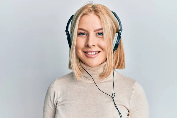 若いですブロンド女性は 正と幸せな立って見てヘッドフォンを使用して音楽に耳を傾け 自信を持って笑顔で歯を示す — ストック写真