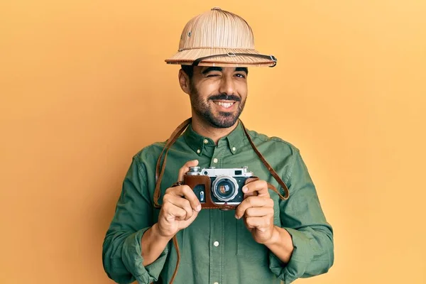若いですヒスパニック男身に着けています探検家の帽子とヴィンテージカメラウインク見ますザ カメラとともにセクシー表現 陽気で幸せな顔 — ストック写真