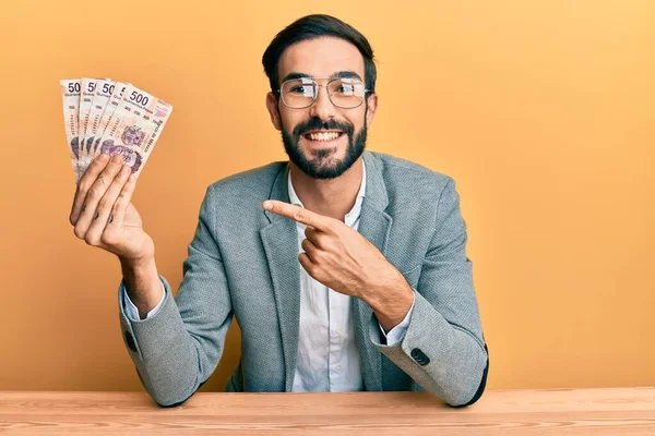 Joven Hispano Sosteniendo Pesos Mexicanos Sentado Mesa Sonriendo Feliz Señalando —  Fotos de Stock