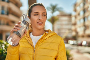Gevşek yüzlü genç İspanyol kız şehirde bir şişe su içiyor..