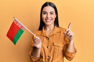 Elinde Belarus bayrağı olan genç esmer bir kadın bir fikir veya soruyla gülümsüyor ve mutlu bir yüzle işaret ediyor. 