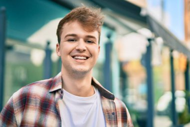 Genç beyaz adam gülümseyerek şehirde mutlu mesut duruyor..