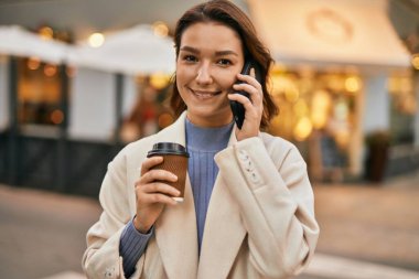 Genç İspanyol kadın gülümsüyor. Şehirdeki akıllı telefondan konuşuyor..