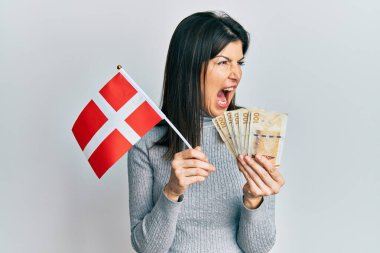 Genç İspanyol kadın elinde Danimarka bayrağı ve Krone banknotları tutuyordu kızgın ve öfkeli çığlıklar atıyordu öfkeyle bağırıyordu. öfke ve agresif konsept. 