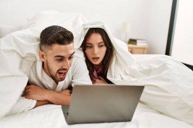 Yatakta dizüstü bilgisayar kullanarak film izleyen genç İspanyol çift..