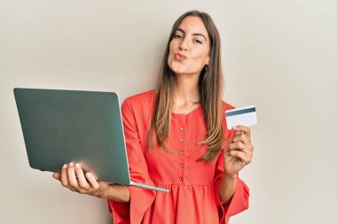 Genç, güzel bir kadın dizüstü bilgisayar ve kredi kartı tutuyor ve kameraya bakıyor. Öpücük yolluyor, güzel ve seksi. aşk ifadesi. 