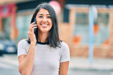 Genç İspanyol kadın gülümsüyor. Şehirdeki akıllı telefondan konuşuyor..