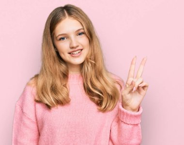 Güzel, genç, beyaz bir kız, sıradan bir kazak giyiyor. İki numarayı gösteriyor ve gülümsüyor. Kendinden emin ve mutlu.. 