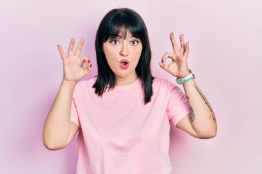 Gündelik kıyafetler giyen genç İspanyol kadın şaşırmış ve şok olmuş görünüyor. Tamam sembolünü parmaklarıyla yapıyor. çılgın ifade 