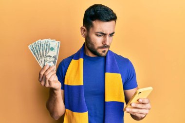 Genç İspanyol futbolcu Amerikan dolarlarını elinde tutan akıllı telefon destekçisi şüpheci ve sinirli, sorun yüzünden üzgün. negatif kişi. 