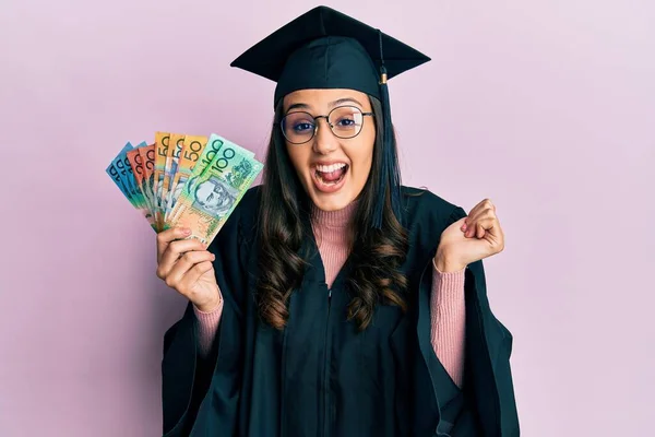 Young Hispanic Woman Wearing Graduation Uniform Holding Australian Dollars Screaming — Stock Photo, Image