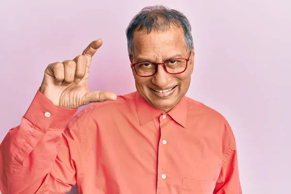 印度中年男子 身穿休闲装 戴着眼镜 微笑着 自信地摆姿势 手拿着小尺寸的标志 手拿着手指 手拿着相机 计量概念 — 图库照片
