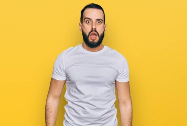 Sakallı, sıradan beyaz tişörtlü genç adam şaşkınlık ve şaşkınlık dolu bir ifade, korku ve heyecan dolu bir yüz.. 