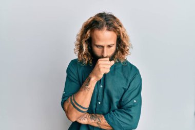 Sakallı, uzun saçlı, günlük kıyafetler giyen, kendini iyi hissetmeyen ve soğuk algınlığı veya bronşitin belirtisi olarak öksüren yakışıklı bir adam. sağlık hizmeti kavramı. 