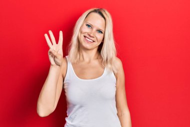 Güzel, beyaz tişört giyen beyaz tenli sarışın kadın üç numarayı gösterip işaret ederken kendinden emin ve mutlu bir şekilde gülümsüyor.. 