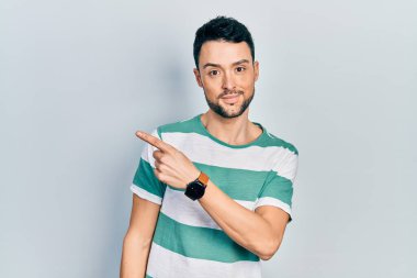 Gündelik giysiler giymiş genç İspanyol bir adam el ile işaret ediyor. Ciddi ve sakin bir yüz ifadesi sergiliyor. 