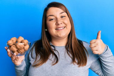 Güzel esmer, elinde cevizli bir kâse tutan, mutlu ve pozitif gülümseyen mükemmel bir baş parmak ve onay işareti olan bir kadın. 