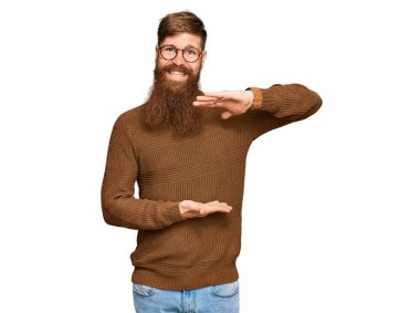 Genç İrlandalı kızıl adam günlük kıyafetler ve gözlük takıyor. Elleriyle işaret ediyor. Ölçü sembolü. Kameraya bakıp gülümsüyor. ölçüm kavramı. 