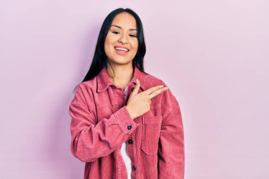 Güzel İspanyol bir kadın, burun piercing 'i takıyor, pembe bir ceket giyiyor, yüzünde mutlu ve doğal bir ifadeyle elleri ve parmaklarıyla yüzünü gösteren bir gülümseme var. 