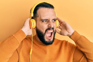 Sakallı genç adam kulaklık takıp müzik dinliyor öfkeli ve öfkeli çığlıklar atıyor öfkeyle bağırıyor. öfke ve agresif konsept. 