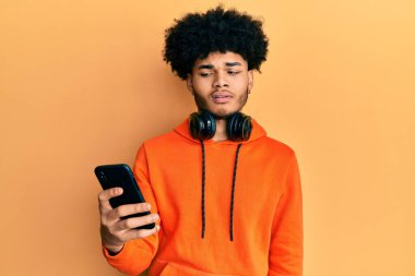 Afro saçlı Afro-Amerikan genç adam akıllı telefondan habersiz ve kafası karışık bir ifade kullanıyor. şüphe kavramı. 