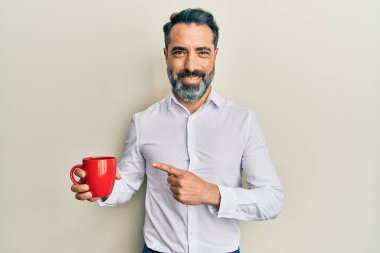 Orta yaşlı, sakallı, kır saçlı kahve içen mutlu, eli ve parmağı olan bir adam. 