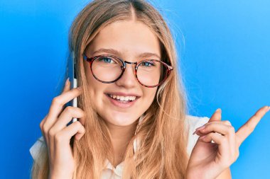 Güzel, genç, beyaz bir kız akıllı telefondan konuşuyor. Gülümsüyor, mutlu bir şekilde elini ve parmağını yana uzatıyordu. 