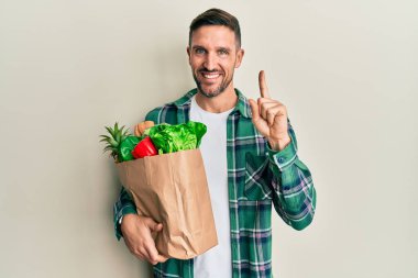 Sakallı yakışıklı bir adam. Elinde poşet, elinde alışveriş poşeti var. Başarılı bir fikirle işaret ediyor. Heyecanlı ve mutlu. Bir numara.. 