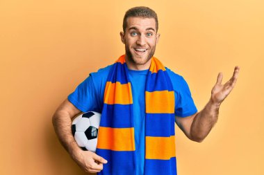 Kafkasyalı genç adam futbol holiganları tezahürat yapıyor zaferi kutlamak için top tutuyorlar mutlu bir gülümsemeyle ve kazanan ifade ellerini kaldırarak 