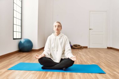 Genç sarışın kız spor merkezinde yoga yapmaya odaklanmış..