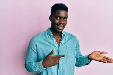 Yakışıklı, sıradan kıyafetler giyen siyah adam kameraya hayret ediyor ve gülümsüyor. Elle ve parmakla işaret ediyor.. 