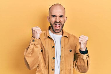 Genç kel adam gündelik giysiler içinde gururla bağırıyor, zaferi kutluyor ve kollarını kaldırarak başarıyı kutluyor. 