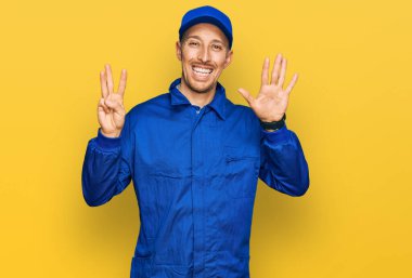 Sakallı, inşaatçı tulumu giyen kel bir adam sekiz numaralı parmaklarıyla kendini gösterip gülümserken mutlu ve kendinden emin.. 