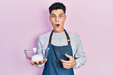 Önlük takan genç İspanyol adam elinde ekmek hamuru kasesiyle korkmuş ve ağzı açık şaşkınlıkla şaşırmış, inançsız yüz. 