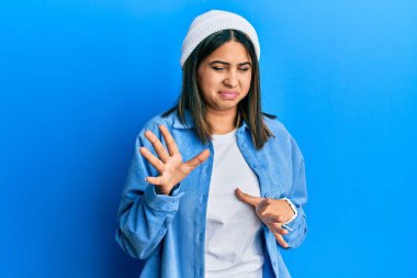 Genç Latin kadın şirin yün şapkalı, tiksindirici bir ifade takınıyor, tiksindirici bir ifade takınıyor ve tiksindirici bir ifade takınıyor.. 