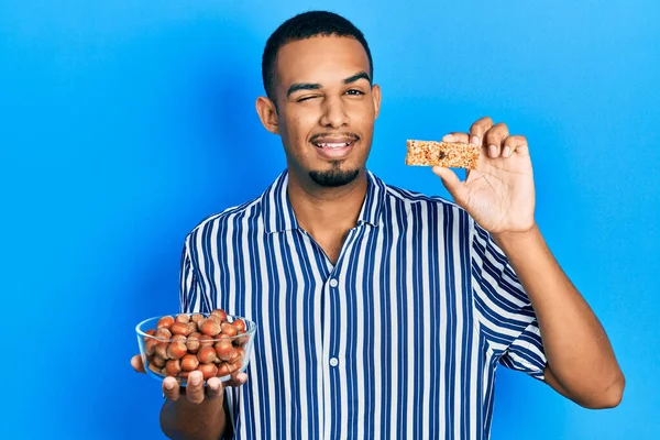 Joven Hombre Afroamericano Sosteniendo Avellanas Crudas Barra Cereal Guiño Mirando — Foto de Stock