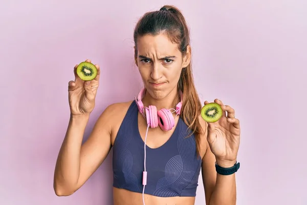 Ung Vacker Kvinna Bär Gym Kläder Hålla Skiva Kiwi Skeptisk — Stockfoto