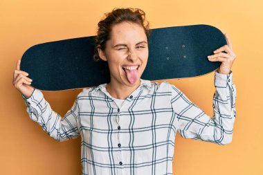 Genç esmer kadın elinde patenle dil uzatıyor. Komik bir ifadeyle mutlu.. 