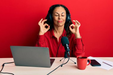 Güzel orta yaşlı bir kadın radyo stüdyosunda çalışıyor rahatlıyor ve gözleri kapalı gülümsüyor parmaklarıyla meditasyon hareketi yapıyor. yoga konsepti. 
