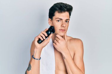 Elektrikli tıraş makinesiyle tıraş olan genç İspanyol adam yüzünde ciddi bir ifadeyle rahatlamış. Basit ve doğal bir şekilde kameraya bakıyorsun.. 