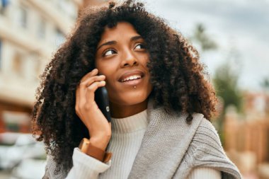 Genç Afrikalı Amerikalı kadın gülümsüyor. Şehirdeki akıllı telefondan mutlu bir şekilde konuşuyor..