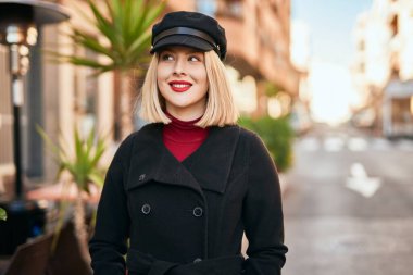 Genç sarışın kadın gülümsüyor, mutlu bir şekilde şehirde duruyor..