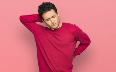 Sıradan kıyafetler giyen, boynu ağrıyan, eliyle boynuna dokunan, kas ağrısı çeken genç yakışıklı bir adam. 